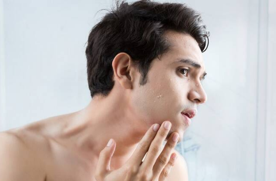 A man with acne looking at his face in mirror